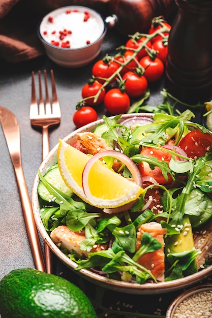 Fresh Salad with chicken tomatoes arugula onion avocado sesame seeds and lemon oil dressing Healthy food Top view Brown table