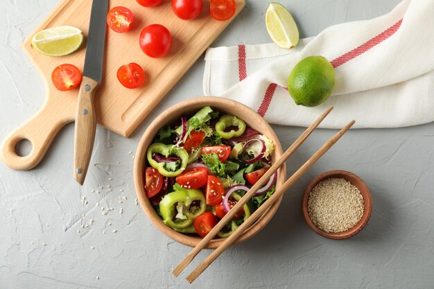 Fresh salad with chopsticks and kitchen accessories on grey