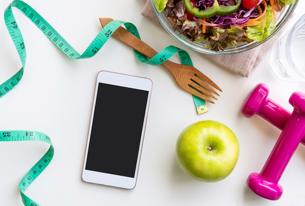 Photo fresh salad with green apple, dumbbell, measuring tape and empty screen smartphone