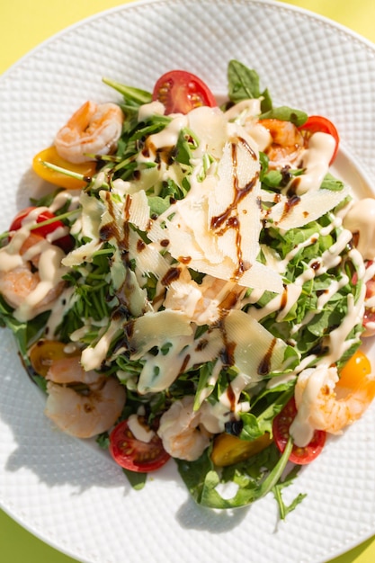 Fresh salad with greens tomatoes grilled shrimps on white plate Top view on yellow background