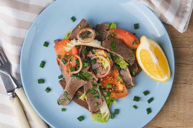 Fresh salad with pork heart lettuce tomato green onion and lemon in blue plate on wooden table