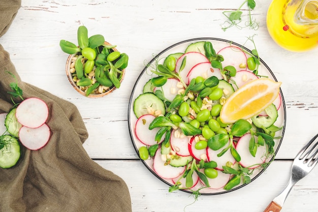 Fresh salad with radish cucumber green pea sunflower soy and mung bean sprouts edamame and flax seeds Vegetarian vegan healthy food Top view old white kitchen table