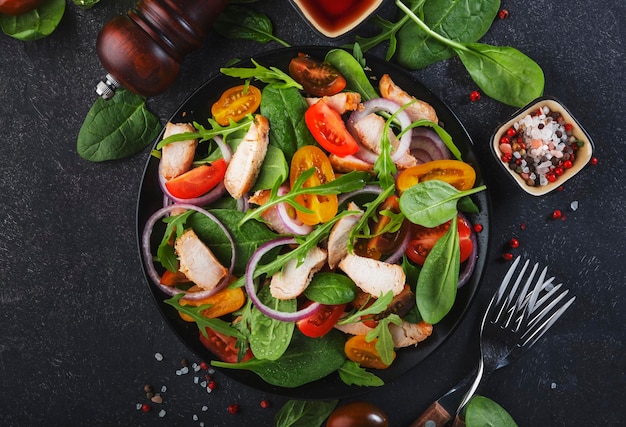 Fresh salad with spinach chicken tomatoes arugula corn lettuce and onion Healthy food Black table