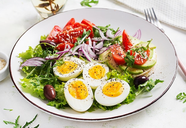 Fresh salad with tomato olives boiled eggs and and sandwich with ricotta cheese avocado