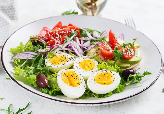 Fresh salad with tomato olives boiled eggs and and sandwich with ricotta cheese avocado