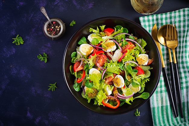 Fresh salad with vegetables tomatoes, red onions, lettuce and quail eggs. Healthy food and diet concept. Vegetarian food. Top view, overhead