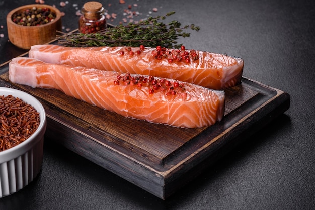 Fresh salmon fillets on black cutting board with herbs and spices