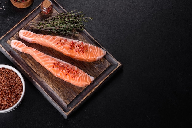 Fresh salmon fillets on black cutting board with herbs and spices