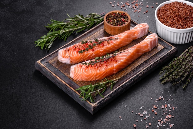 Fresh salmon fillets on black cutting board with herbs and spices