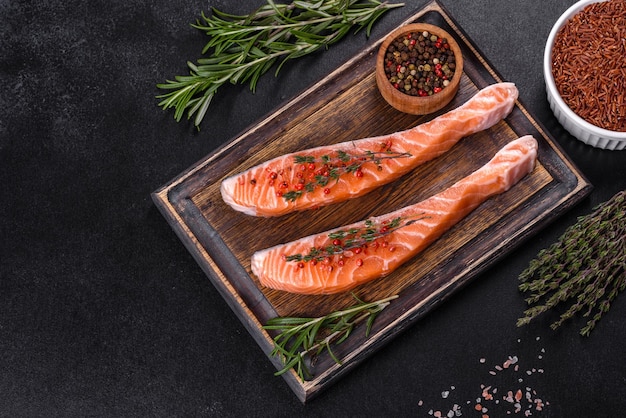 Fresh salmon fillets on black cutting board with herbs and spices