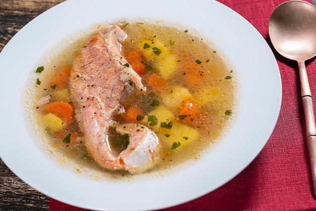 Fresh salmon fish soup with carrots and potatoes in a white plate close up