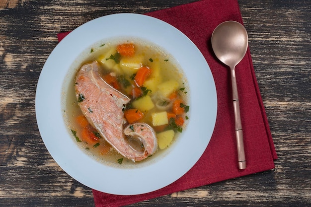 Fresh salmon fish soup with carrots and potatoes in a white plate close up