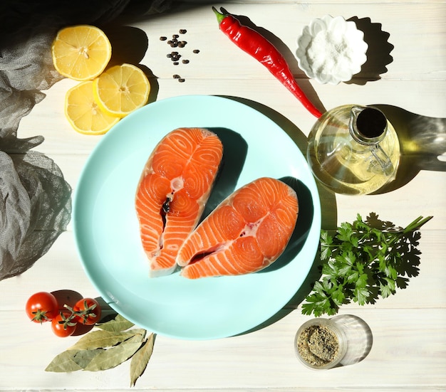 Fresh salmon steak with ingredients onblue plate and white wooden background