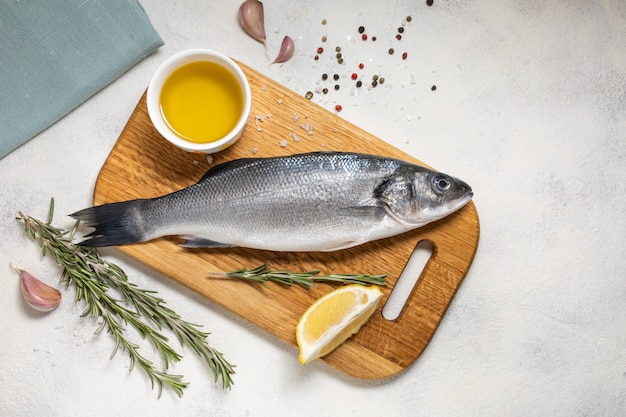 Fresh sea bass fish and ingredients for cooking, lemon and rosemary. White background top view.