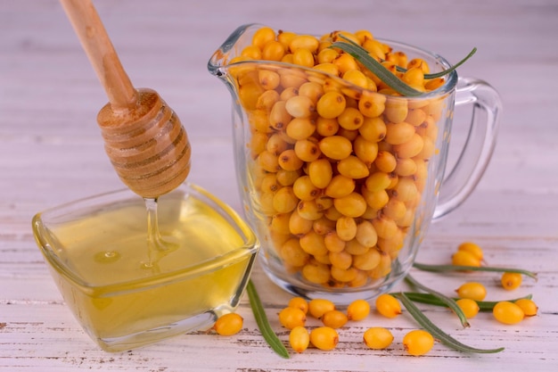 Fresh sea buckthorn berries in a decanter and honey on a white wooden