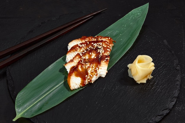 Fresh seafood sashimi smoked eel on slate board with wasabi and ginger on black background