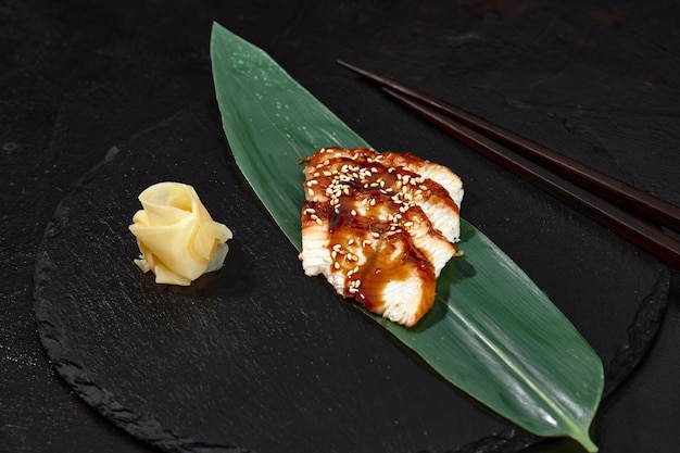 Fresh seafood sashimi smoked eel on slate board with wasabi and ginger on black background