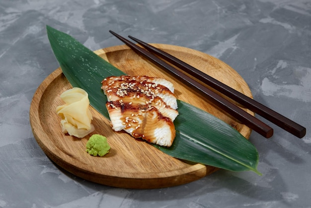 Fresh seafood sashimi smoked eel on slate board with wasabi and ginger on black background