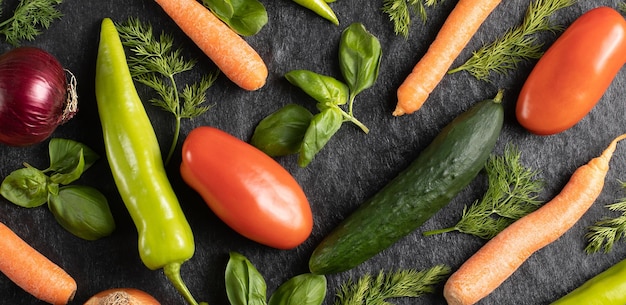 Fresh seasonal vegetables green pepper tomato onion carrot cucumber basil dill on gray black background top view