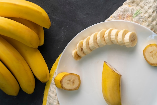 Fresh sliced banana in a white ceramic plate on the black table, preparing ingredients for healthy breakfasts