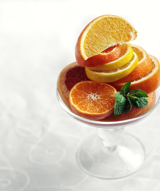 fresh sliced citrus fruits with mint in glass vase on white background