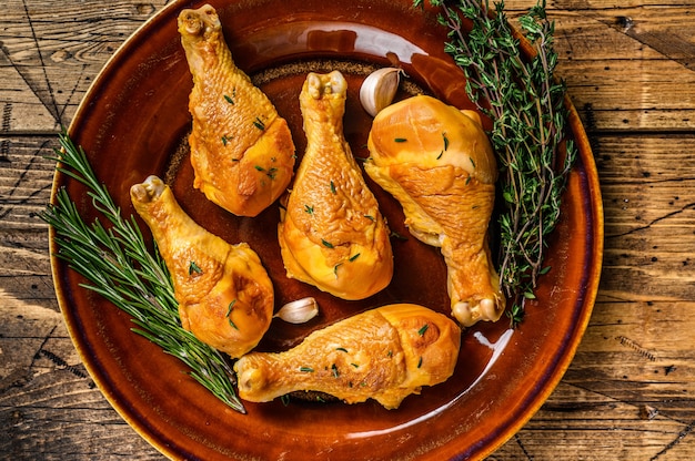 Fresh Smoked chicken drumsticks on a rustic plate with herbs on wooden table. Top view.