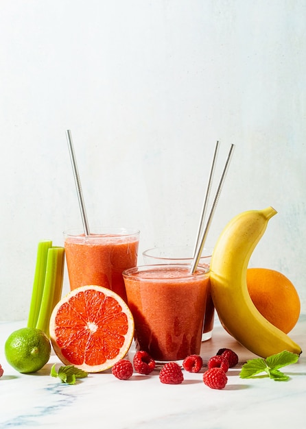 Fresh smoothie juice in glasses with metal tubes on the table and ingredients.