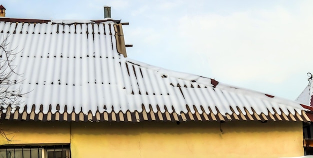 Fresh snow on the roof of the old wavy asbestoscement slate against the sky