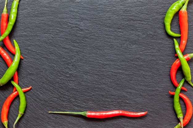 Fresh spicy red and green pepper on a slate board, various colorful chili peppers and cayenne peppers on dark background from above. Top view, copy space.