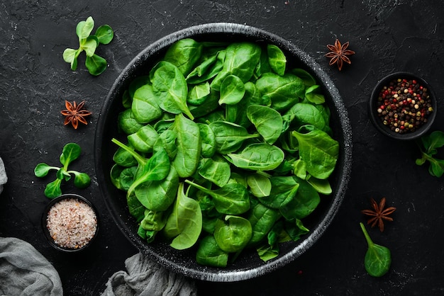 Fresh spinach In a black plate on a wooden background Top view Free space for your text Flat lay