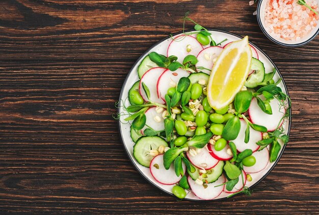 Fresh spring salad plate with radish cucumber green pea sunflower soy and mung bean sprouts edamame and flax seeds Vegetarian vegan healthy food Top view wooden kitchen table