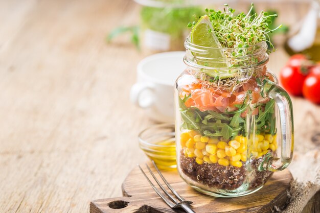 Fresh spring salad with salmon, quinoa, arugula, cress salad and corn in a mason jar.