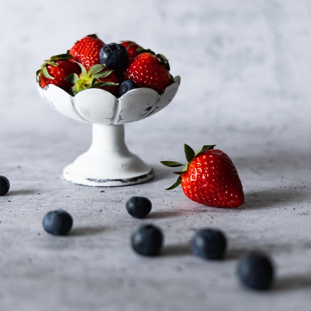 Fresh strawberries and blueberries in a white dessert dish on a gray background