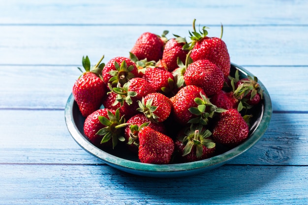 Fresh strawberries in green plate on blue wooden table with beautiful flare and shadow