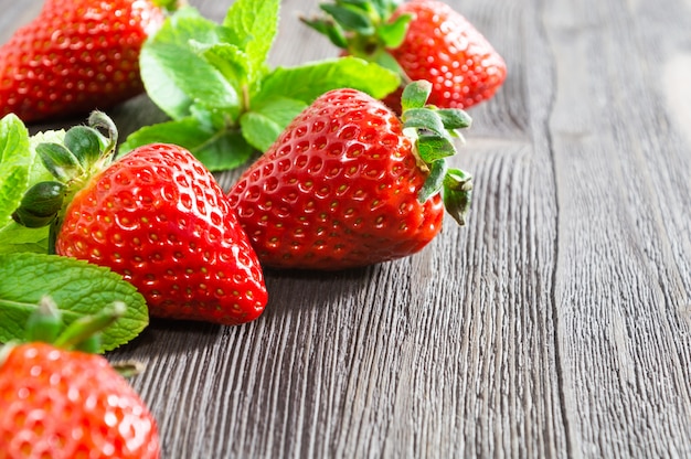 Fresh strawberries and mint leaves on wooden background.