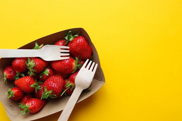 Fresh strawberries in a paper, biodegradable utensils on a yellow background