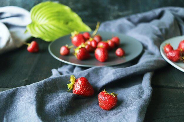 Fresh strawberries on a plate, against the background of green leaves and gray linen fabric 
