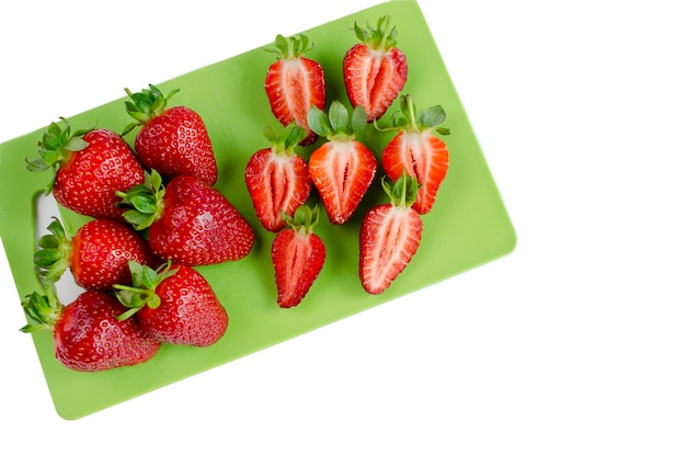 Fresh strawberries sliced on the small green board isolated on the white background flat lay