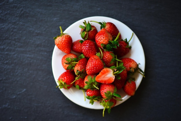 Fresh strawberries on white plate on the table, Red ripe strawberry on dark background