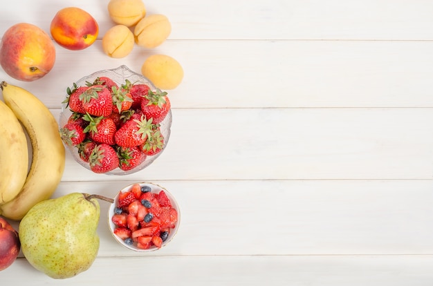 Fresh strawberries with fruits on a white wooden background with copy space. Ingredients for fruit salad.