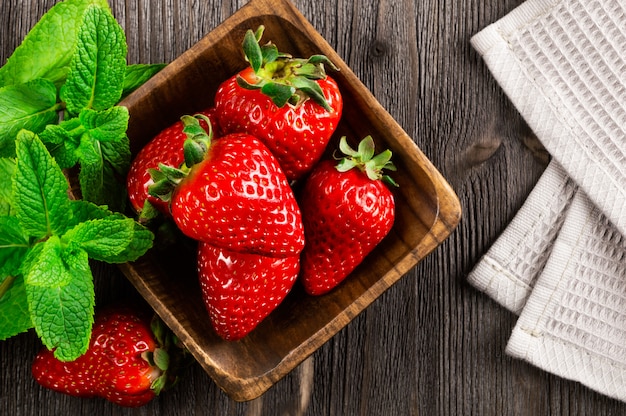 Fresh strawberries in wooden bowl and mint leaves on wooden background. 