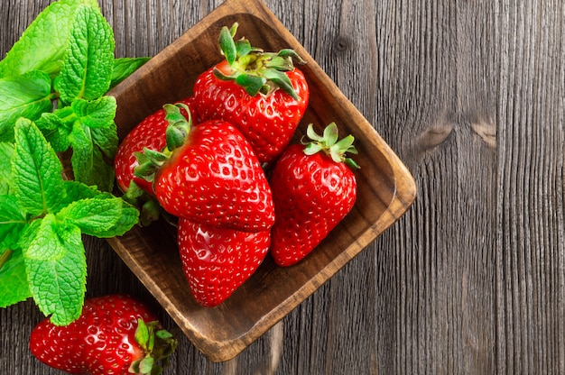 Fresh strawberries in wooden bowl and mint leaves on wooden background