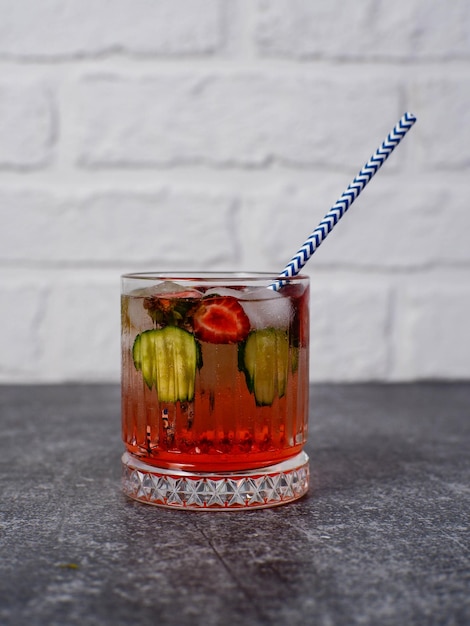 Fresh strawberry cocktail with straw berries with pieces of cucumber and with ice on a gray and bricks background