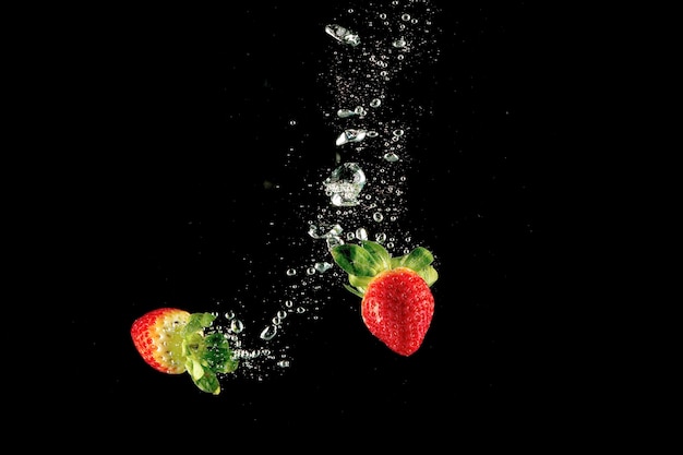 Fresh strawberry dropped into water with splash on isolated black background.