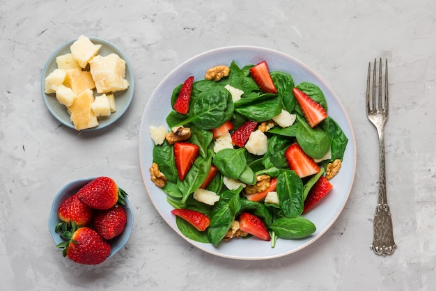 Fresh strawberry salad with spinach leaves, parmesan cheese and walnuts with fork. healthy keto diet food