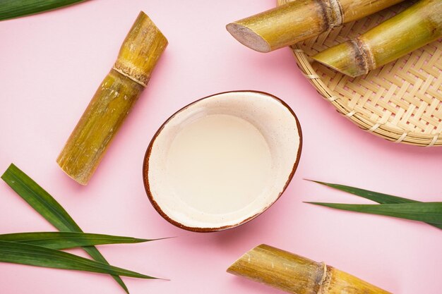 Fresh sugar cane juice and sugar cane on a pink background top view