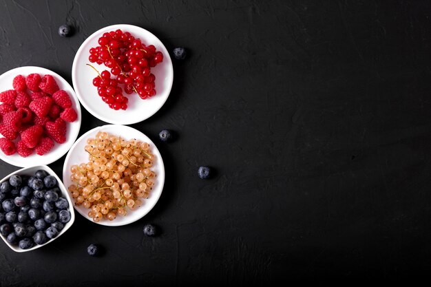 Fresh summer berries in vintage mug over black background, top view