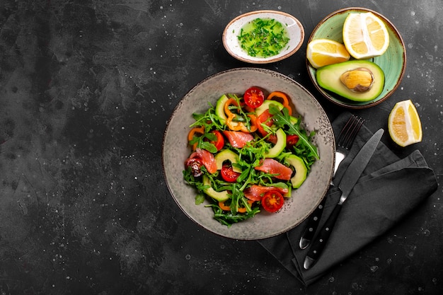 Fresh summer vegetable salad with arugula, tomatoes, bell peppers, avocado and salmon on a plate top view.