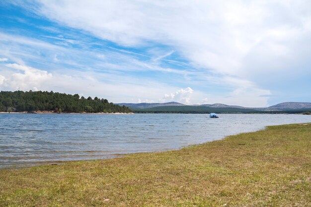 Fresh and summery landscape with a large river surrounded by nature and a small yacht in the middle of the water.