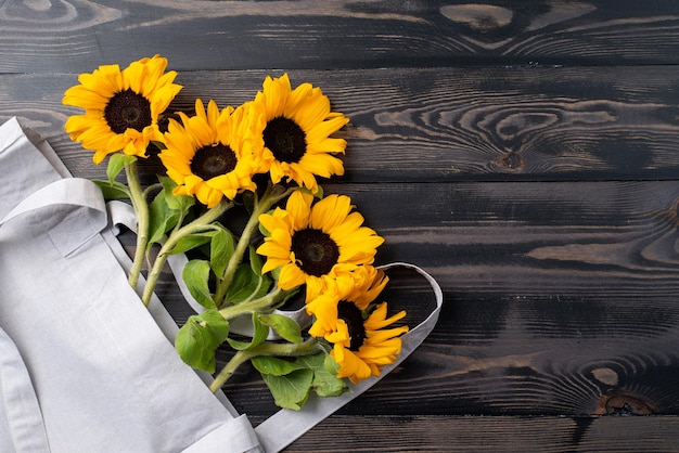 Fresh sunflowers with leaves on stalk in shopping bag on wooden background flat lay top view copy sp